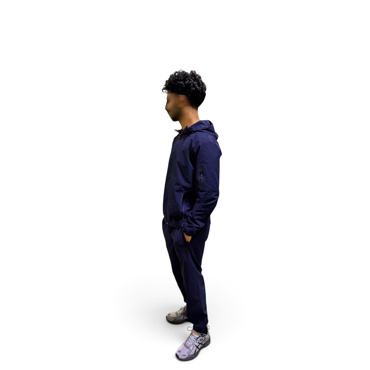 A man wearing a navy blue hooded sweatshirt and matching sweatpants, standing in profile against a solid white background.