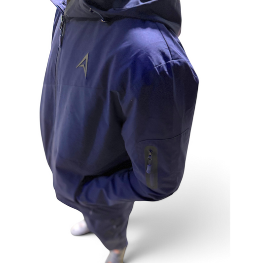 A person wearing a navy blue hooded jacket with a small metallic logo on the chest and a zippered sleeve pocket, photographed against a clean white studio background.