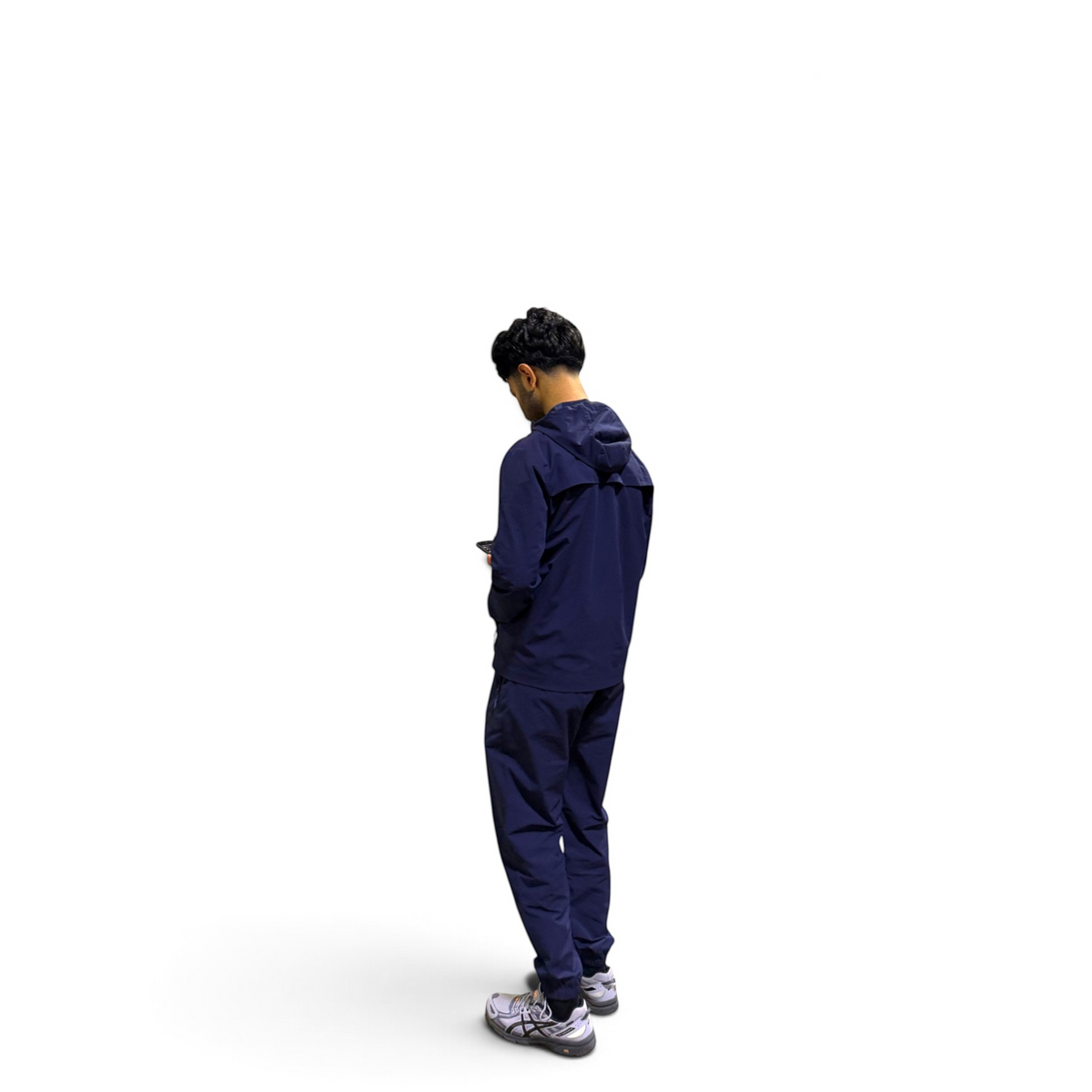 A man wearing a matching navy blue hooded jacket and jogger pants set, viewed from behind as he looks down at a phone, against a solid white background.