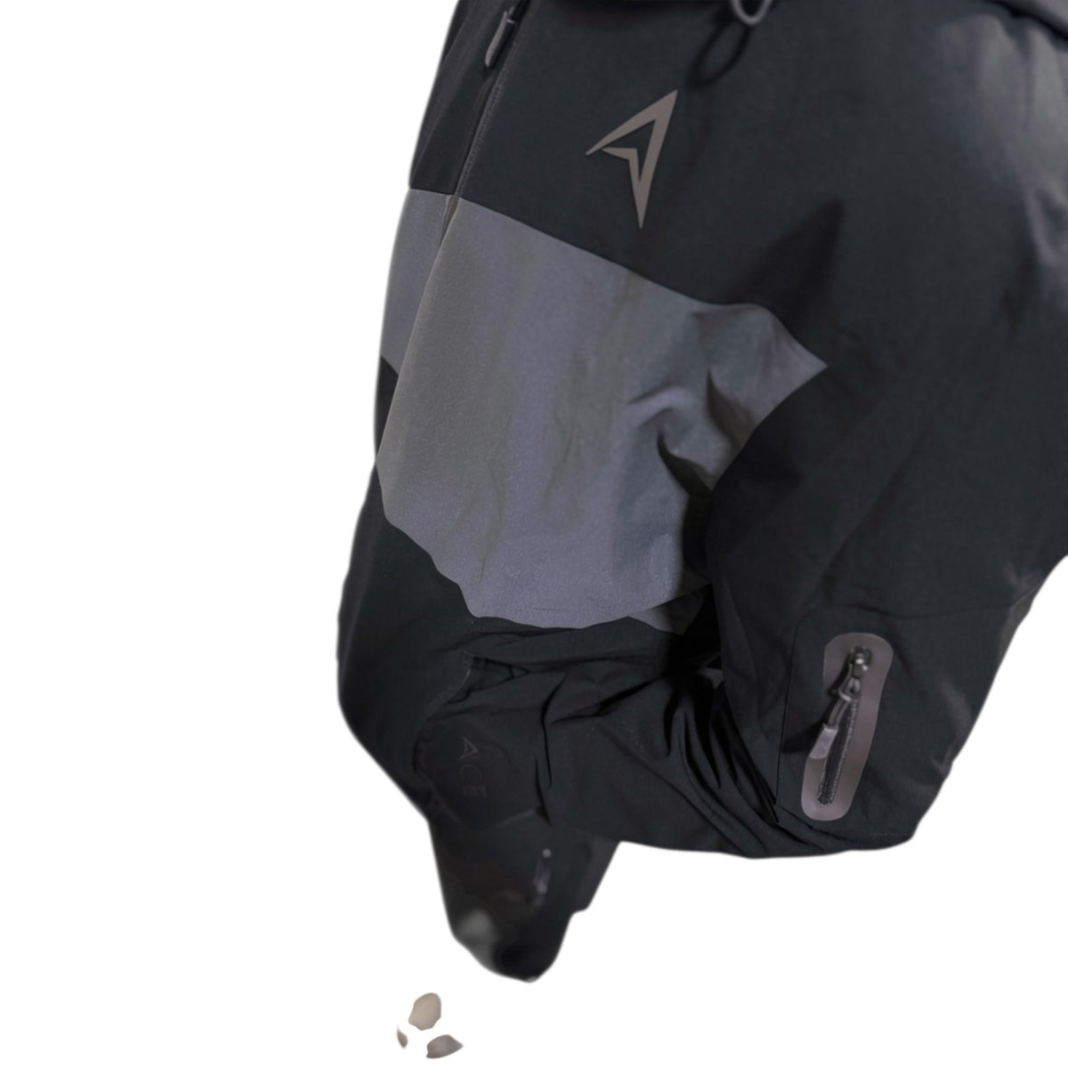 Close-up of a black and gray outdoor jacket sleeve with a gray reflective-looking triangular logo on the upper chest and a zippered pocket on the lower arm, isolated on a white background.